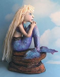 a ceramic statue of a mermaid sitting on top of a rock in front of a blue background