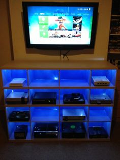 a television sitting on top of a wooden shelf filled with remotes in front of a flat screen tv