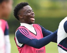 a young man laughing while holding a soccer ball in front of other men on a field