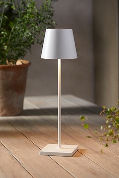 a white lamp sitting on top of a wooden floor next to a potted plant