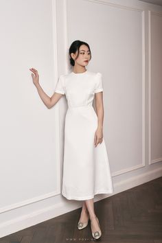 a woman in a white dress leaning against a wall with her hand on the side