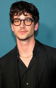 a man wearing glasses standing in front of a blue wall