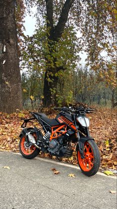 an orange and black motorcycle parked on the side of a road next to a tree