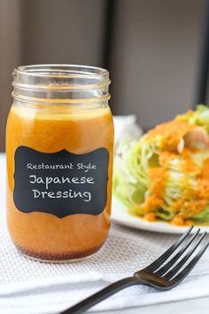 a jar of japanese dressing next to a plate with salad and fork on the table