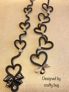 a necklace made out of black wire with hearts and bows on the end, hanging from a hook