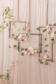 two frames with flowers and greenery hanging on the wall next to each other in front of a pink curtain