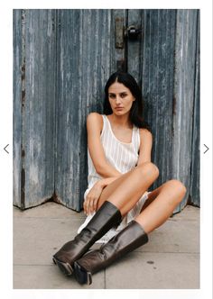 a woman sitting on the ground with her legs crossed, wearing boots and white dress