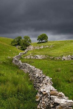 a stone wall in the middle of a grassy field under a dark sky with storm clouds