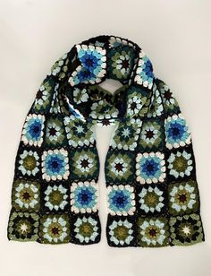 a crocheted scarf with blue and green flowers on the front, sitting on a white surface