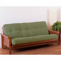 a green futon couch sitting on top of a hard wood floor next to a potted plant