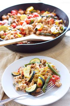 a white plate topped with food next to a skillet filled with rice and vegetables