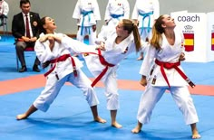 two women are practicing karate on a blue mat while others watch from the sidelines