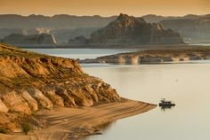 a boat floating on top of a lake surrounded by rocky mountains and desert landscape in the background