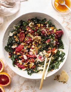 a white bowl filled with salad next to sliced blood oranges and two gold spoons