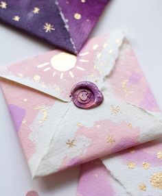 an origami envelope with a pink and purple flower on it, sitting next to other folded paper