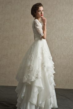 a woman in a white wedding dress standing with her hand on her chin and looking off to the side