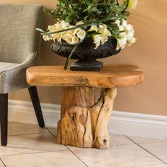 a wooden table topped with a vase filled with flowers next to a chair and wall