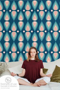 a woman sitting on a bed in front of a wallpaper with an abstract design