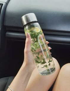 a woman sitting in the back seat of a car holding up a water bottle filled with plants