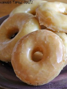 three glazed donuts on a plate with the top one sitting up in front of them