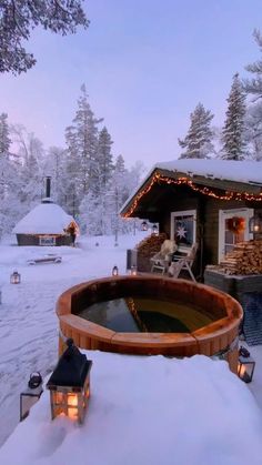 a hot tub sitting in the middle of a snow covered field next to a cabin