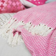 a pink and white blanket sitting on top of a bed next to pillows with decorative designs