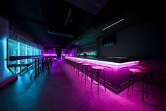 a dimly lit bar with stools and neon lights on the walls, along with purple lighting