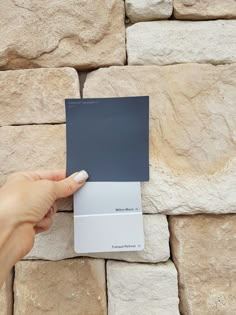 a hand is holding up a gray and white color swatch against a stone wall