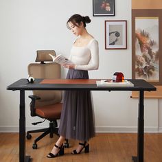 a woman standing in front of a desk reading a book while wearing heels and a white top