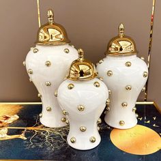 three white vases with gold accents on a table