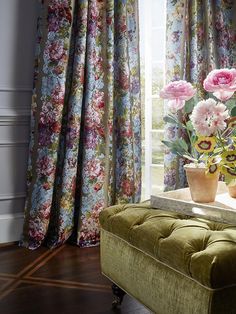 a green bench sitting in front of a window filled with pink and white flowers on top of a wooden floor