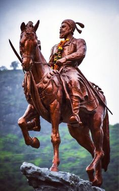 a statue of a man riding on the back of a horse next to a lush green hillside