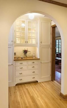 an archway leads into a kitchen with white cabinets and wood floors, along with hardwood flooring