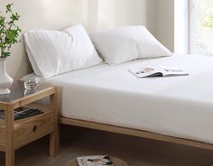 a bed with white sheets and pillows next to a wooden table in front of a window