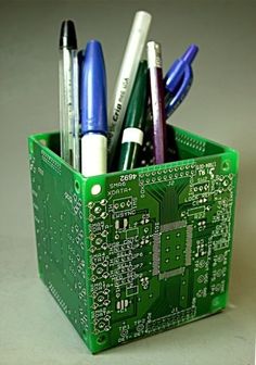 a green container filled with pens and other electronic devices on top of a table next to a computer chip