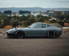 a grey sports car parked on the side of a road in front of a city