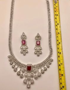 Add elegance to any outfit with our CZ American Diamond Necklace. The sparkling ruby stones add a touch of glamour, making it perfect for any occasion. Our high-quality CZ stones provide the look of real diamonds without the high price tag. Elevate your style with our stunning necklace. This jewellery set includes a necklace and matching earrings. Jewellery Care- Keep the jewellery dry, avoid contact with perfumes and water. Ruby Jewelry With Diamond Accents For Party, Luxury Ruby Necklaces With Diamond Accents, Dazzling Ruby Necklace With Diamond Cut, Luxury Ruby Diamond Necklace With Diamond Accents, Luxury Ruby Necklace With Diamond Accents, Luxury Ruby Diamond Necklace With Accents, Dazzling Ruby Necklace With Sparkling Stones, Ruby Necklaces With Sparkling Stones For Party, Formal Cubic Zirconia Diamond Necklace With Rhinestones