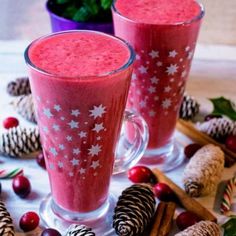 two glasses filled with smoothie sitting on top of a table next to pine cones