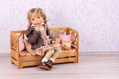 a doll sitting on top of a wooden bench next to a wallpapered background