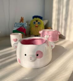 three ceramic cups with pink and white designs on them sitting on a table next to a stuffed animal