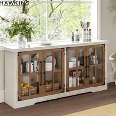 a white and brown cabinet with glass doors in a living room next to a window