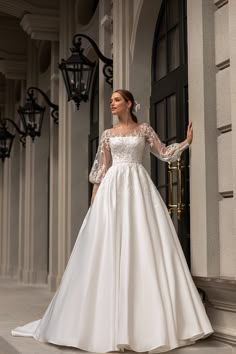 a woman in a white wedding dress standing by a door with her arms out and looking off to the side