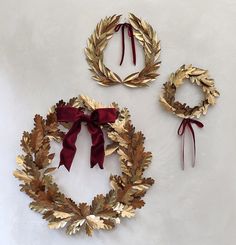 three gold wreaths with red bows and ribbons on a white surface next to each other