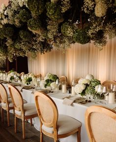 a long table with white flowers and greenery on the ceiling is set for a formal dinner