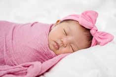 a baby girl is sleeping on a white blanket with a pink bow in her hair