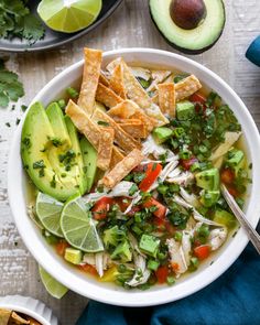 a bowl of chicken tortilla soup with avocado, cilantro and lime