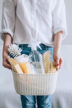 a woman is holding a basket full of cleaning products