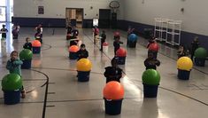 many children are sitting in buckets on the floor with balls around them and one child is holding a basketball hoop