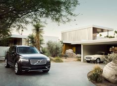 two cars are parked in front of a house with palm trees and rocks on the driveway