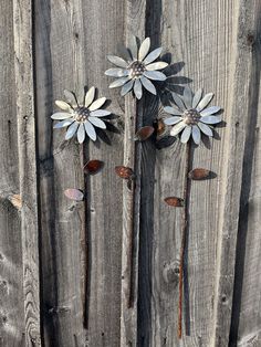 three metal flowers sitting on top of a wooden fence